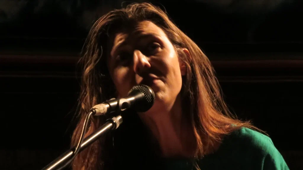 Julia Holter singing at a microphone in warm low light