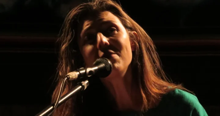 Julia Holter singing at a microphone in warm low light