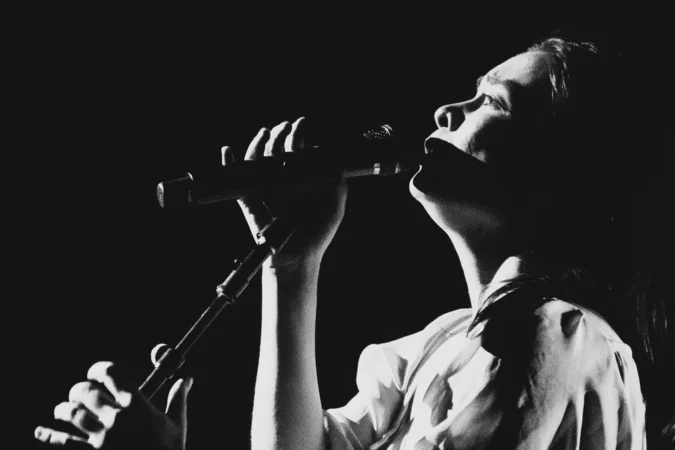 Mitski singing into a handheld microphone, photographed in high-contrast black and white