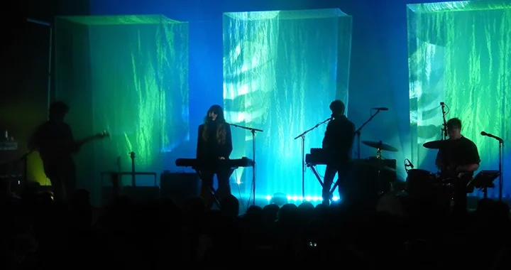 Beach House performing in silhouette against green and blue lit fabric columns