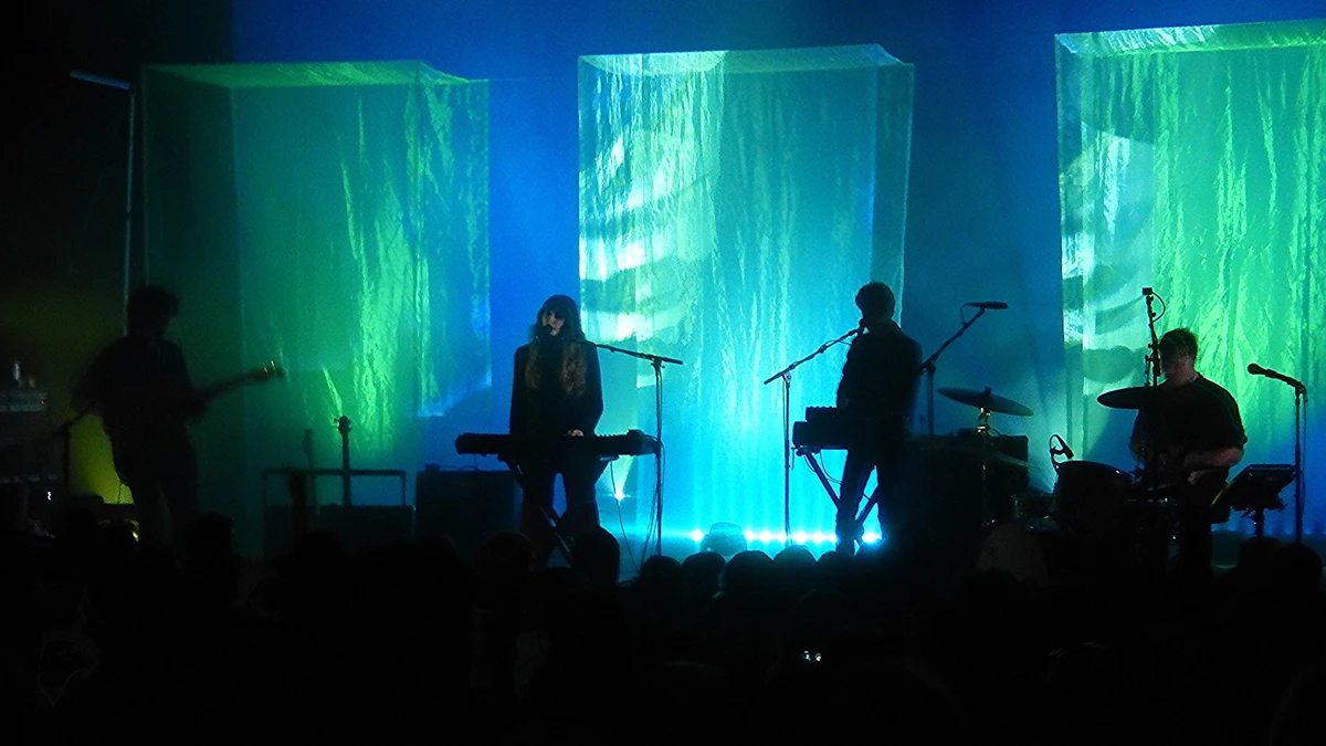 Beach House performing in silhouette against green and blue lit fabric columns