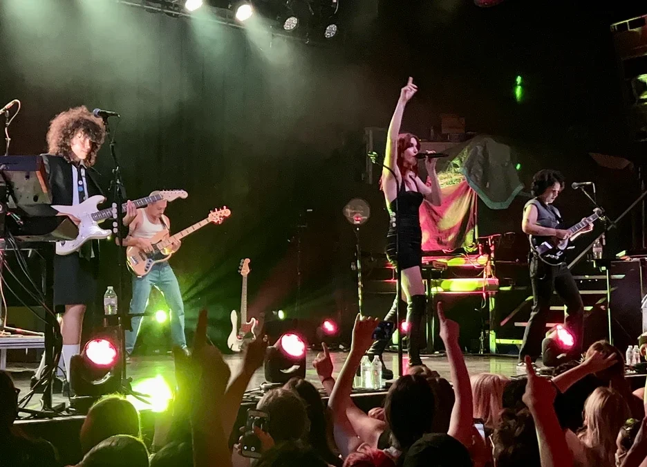MUNA performing on stage with the crowd's hands raised